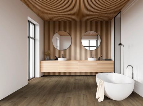 Modern bathroom with wooden paneling, round mirrors, a freestanding bathtub, and sleek fixtures.