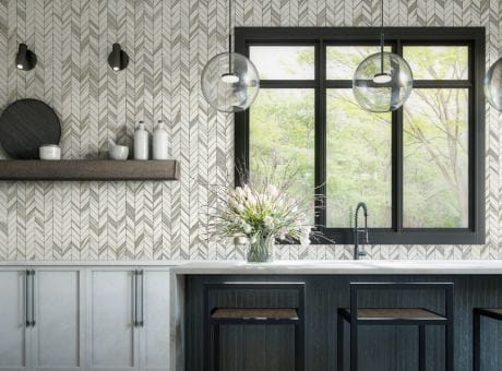 Modern kitchen with chevron tile backsplash, large window, decorative shelf, and flower vase.