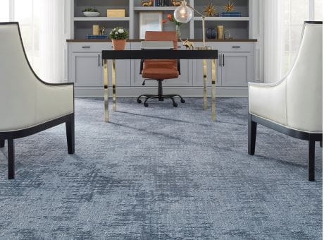 Modern office space with blue Fabrica carpet, white armchairs, a desk, and shelves with decor.