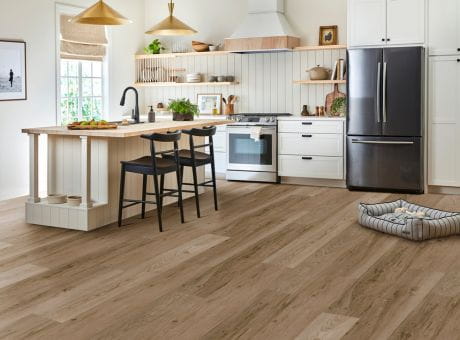 Modern kitchen with wood-style vinyl flooring, central island, and stainless steel appliances.