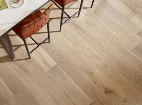 Close-up of a light oak laminate hardwood floor with a table and chair partially visible.