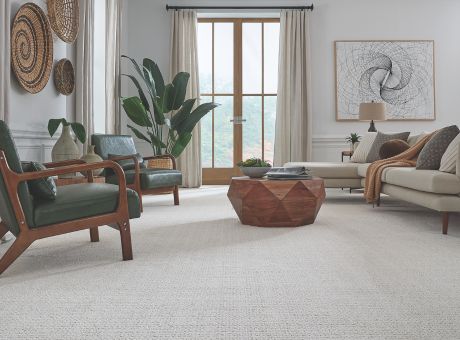 Modern living room with Masland Carpet Purebred, including green armchairs, a wooden coffee table, beige sofa, and woven wall art.