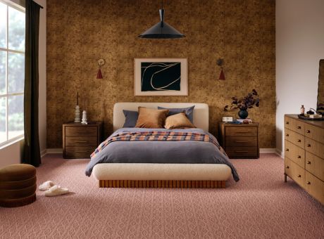 A well-decorated bedroom with a bed in front of a patterned wall and bedside tables, showcasing elegant decor and earthy tones.