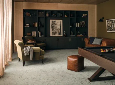 A cozy room with a built-in dark bookshelf, green armchair, leather sofa, pool table, and chess set.