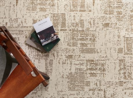 A textured rug displaying an abstract pattern, featuring a stack of books next to a wooden chair.