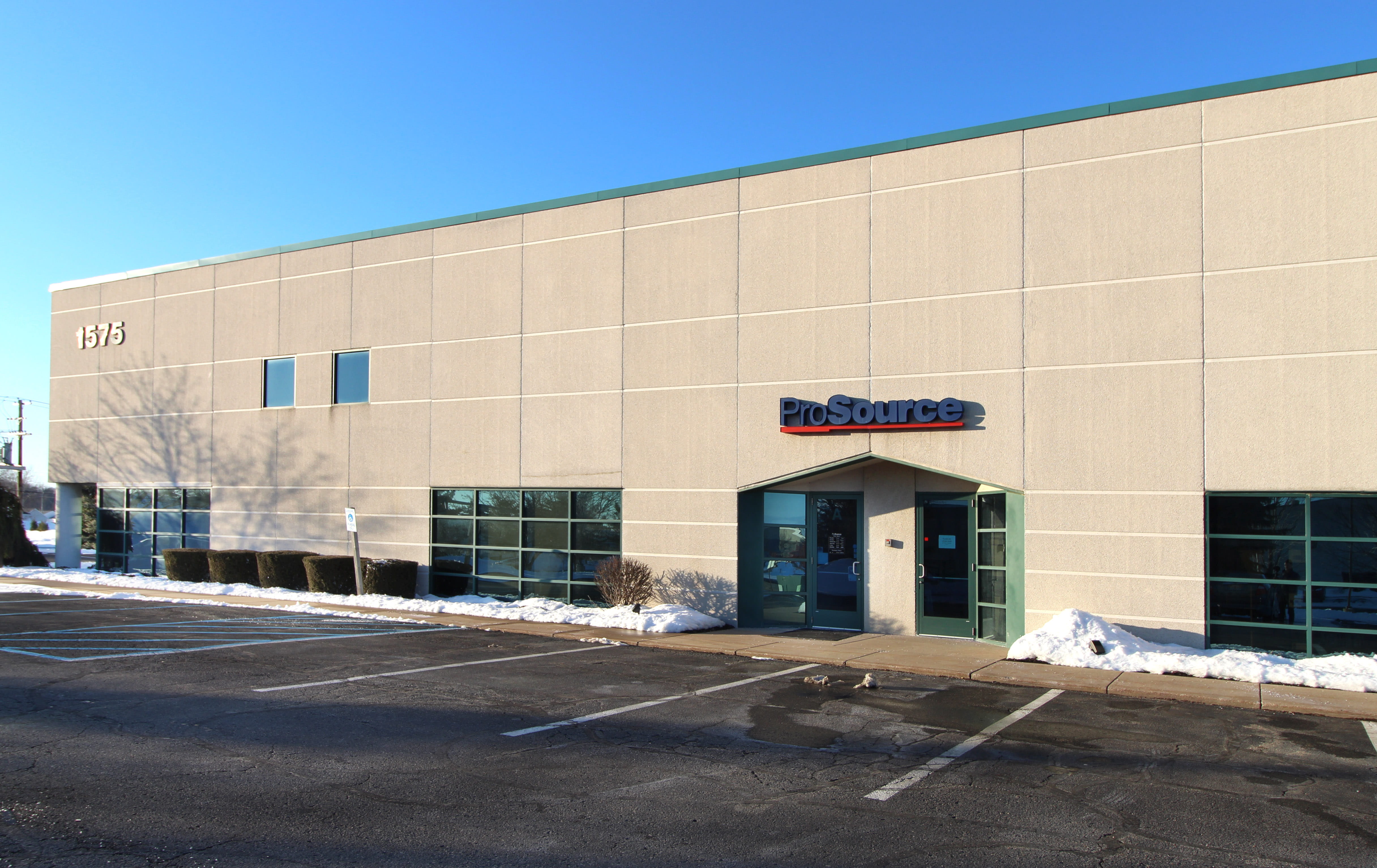 The facade of ProSource building, a beige commercial establishment, with the street number 1575 visible and parking spaces in the front.
