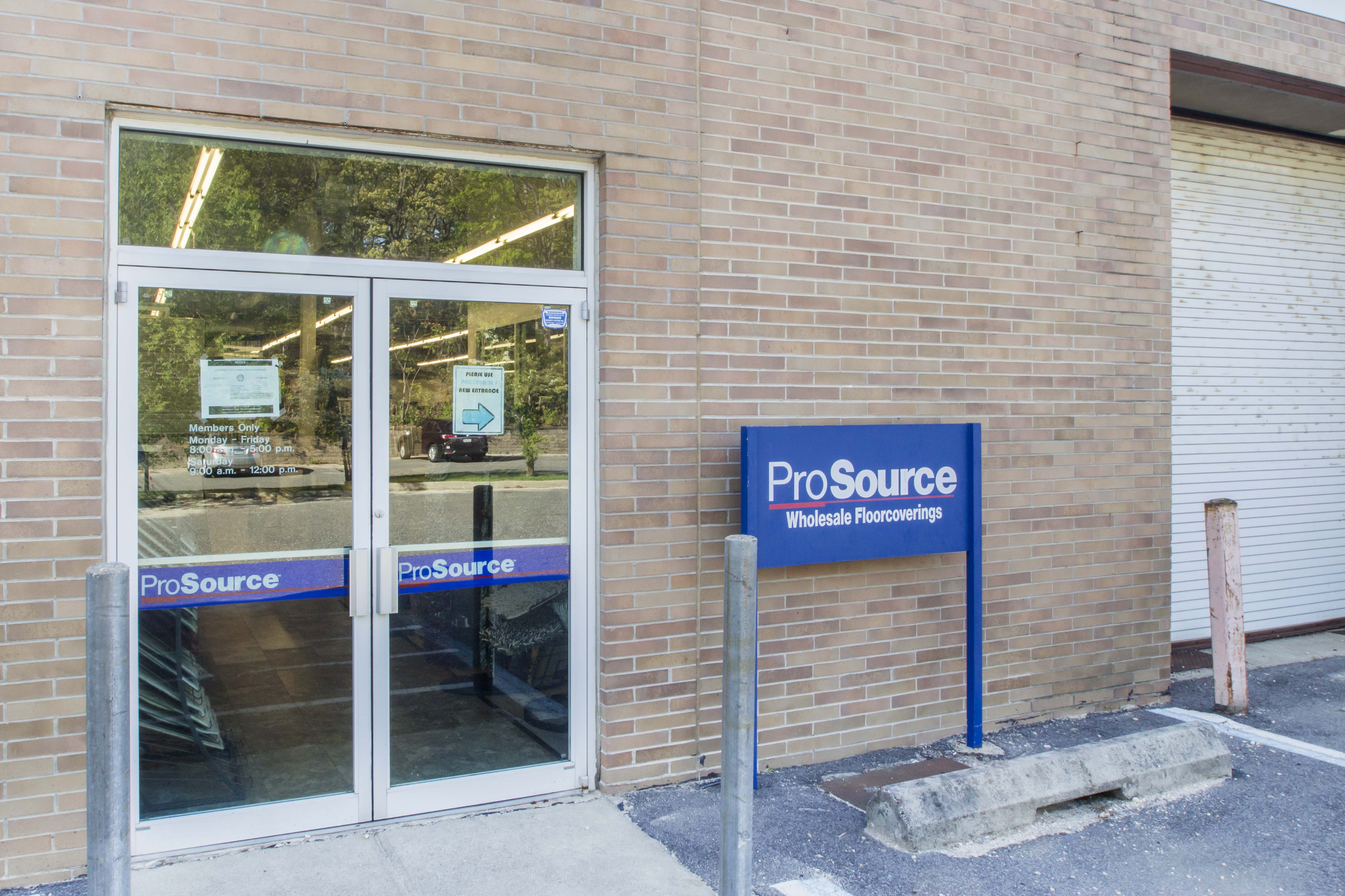 Glass double door entrance of ProSource Wholesale Floorcoverings store with a visible blue sign.