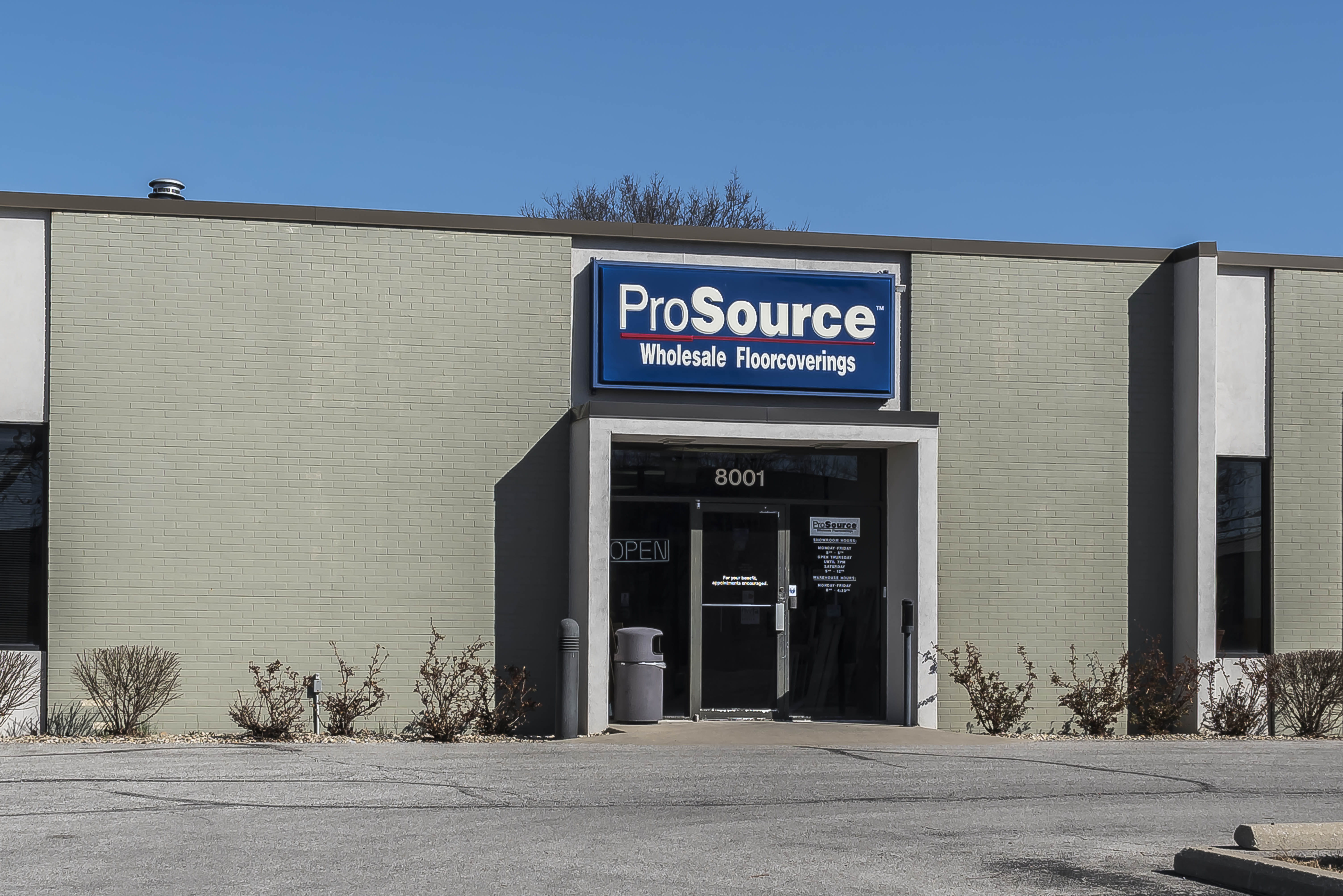 Exterior view of a ProSource Wholesale Floorcoverings store with a green-painted exterior and visible entrance signage displaying the company's name and address.
