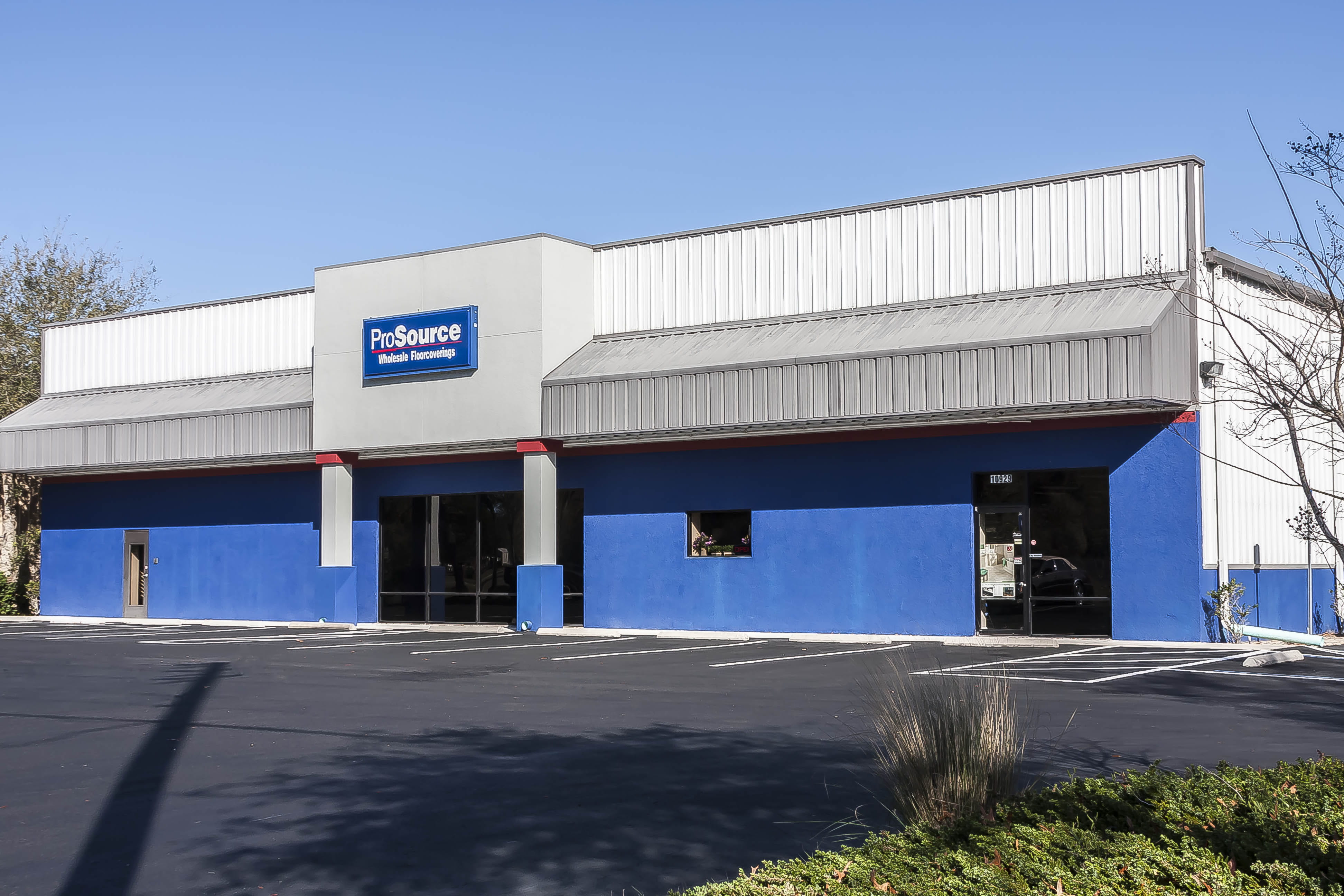 Exterior view of ProSource Wholesale Floorcoverings building with blue and white facade and empty parking lot.