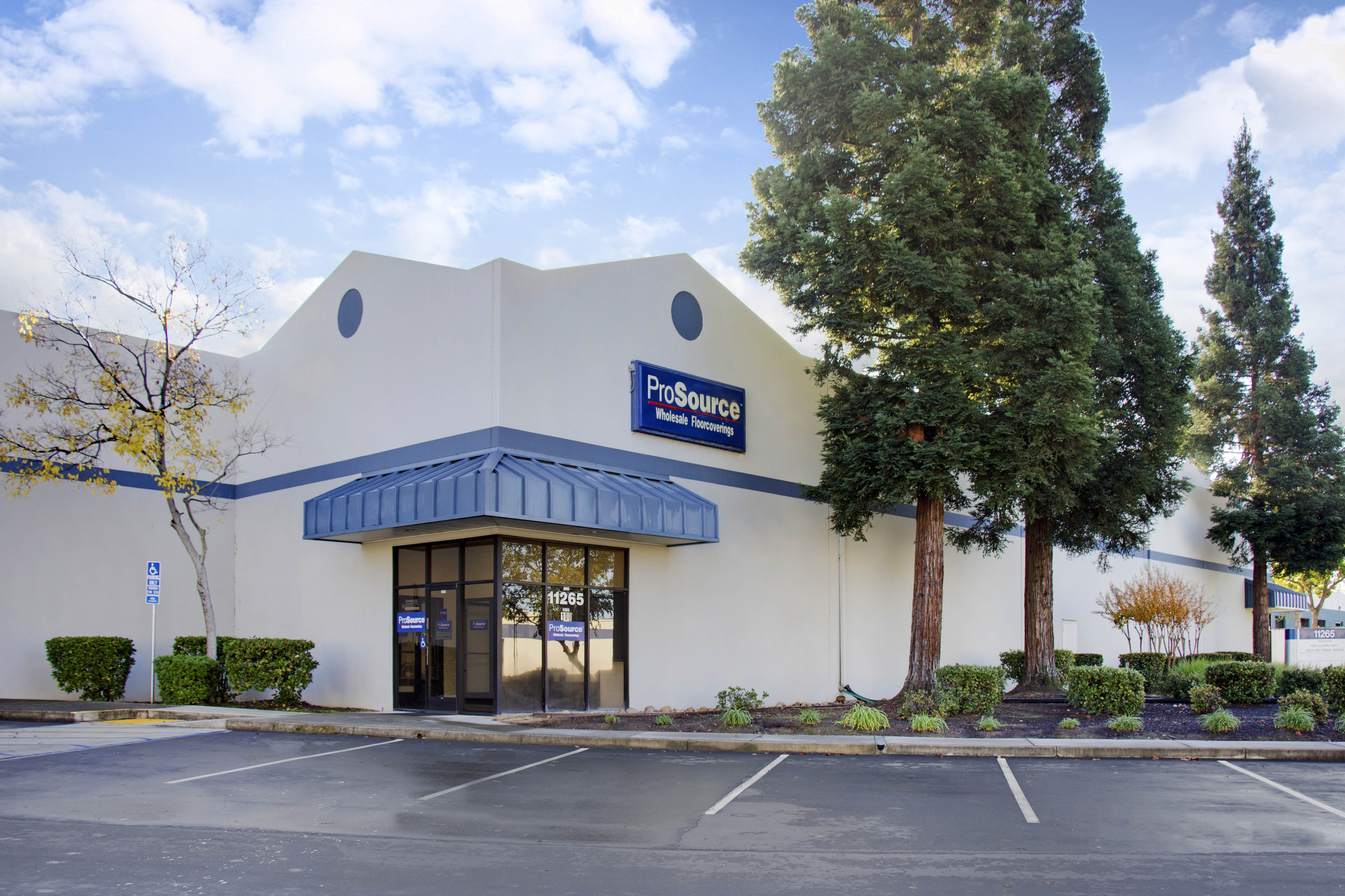 Exterior of ProSource Wholesale Flooring building with signage, trees, and parking spaces.