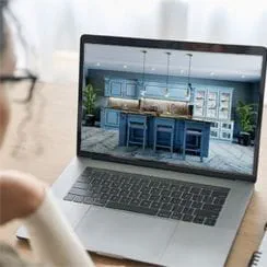 An individual observes a laptop screen showcasing a contemporary kitchen with blue cabinets and an island.