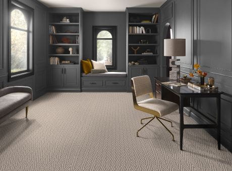 Home office with gray bookshelves, window seat, desk, and herringbone carpet.
