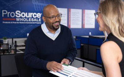 Two people interacting at ProSource Wholesale, reviewing a catalog or material samples in a professional environment.