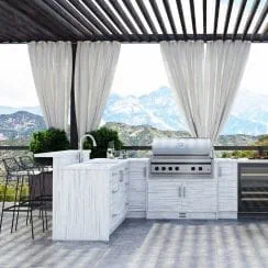 Outdoor luxury kitchen with white marble design, cooking appliances, and mountain scenery background under a pergola with curtains.