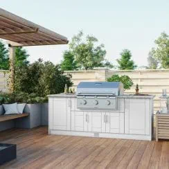 Outdoor kitchen setup with stainless steel grill, weather-resistant cabinetry, wooden patio, and greenery in the background.
