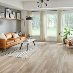 A contemporary living room with wooden floors, brown leather furniture, and large windows with curtains.
