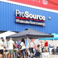 A group of people gathered under a tent outside a ProSource Wholesale Floorcoverings store.