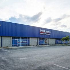 A ProSource Wholesale store with a blue facade and a parking lot in front, taken during the daytime.
