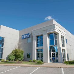 Modern commercial building with large windows and a business sign, surrounded by landscaping.