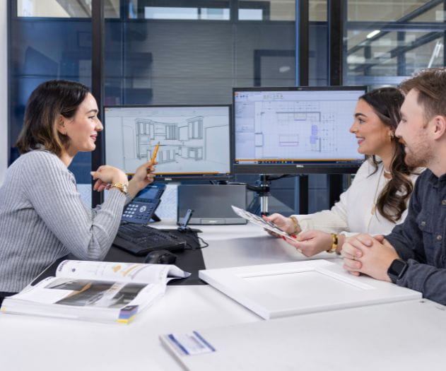 Individuals working together on interior design plans with computers and physical materials in an office setting.