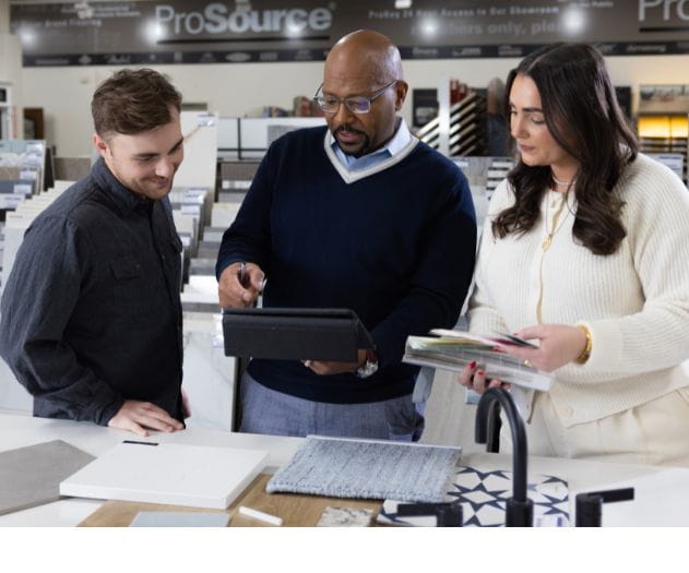 Three people discussing materials and designs at a showroom, displaying tiles and fabric samples on a table.