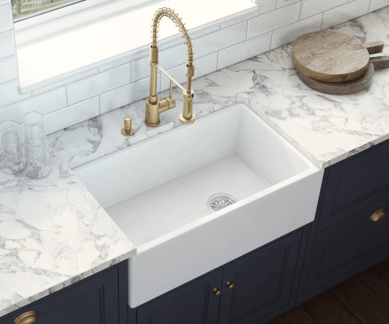 A farmhouse-style kitchen sink with a gold faucet and a marbled countertop.