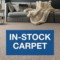 Cozy living room with carpet flooring, a sofa, pillows, throw blanket, and 'In-Stock Carpet' text overlay.