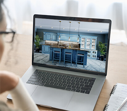 A laptop screen shows a modern blue kitchen design with a person viewed from behind.