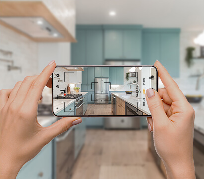 Hands holding a smartphone, with an image of a modern kitchen being displayed on the phone's screen.