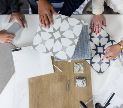 Hands organizing different tiles and materials on a table, showcasing a design selection process.